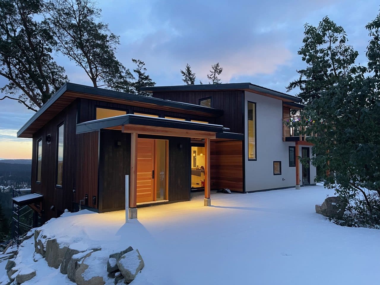 A dark-clad modern home by Nicol Construction at dusk in the snow